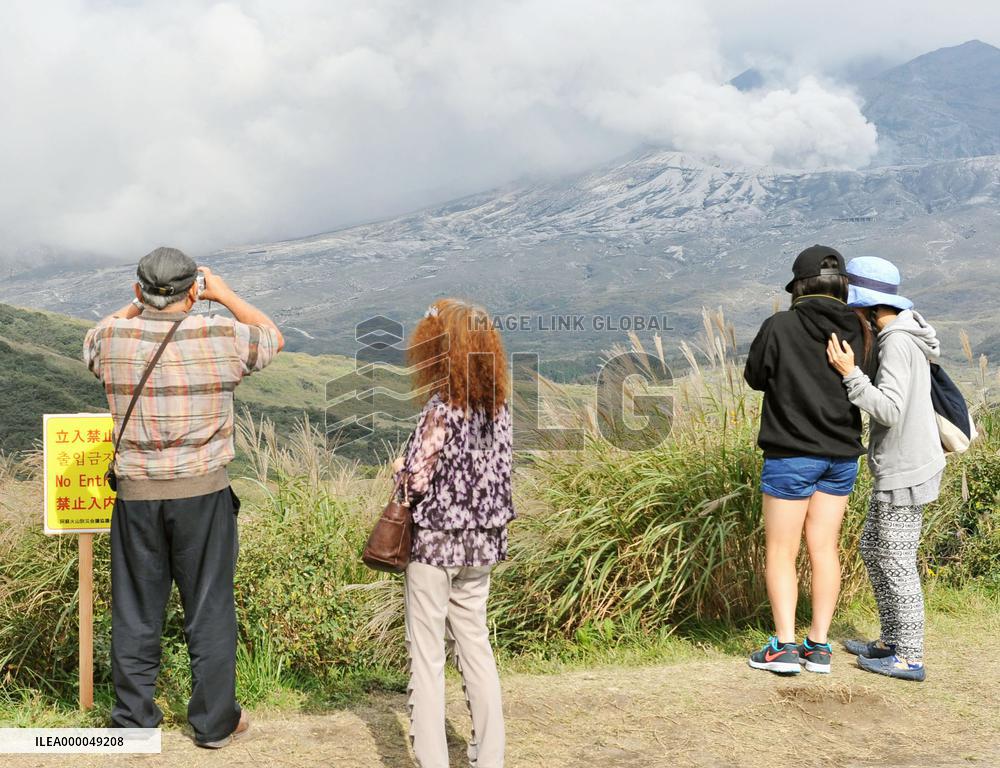 Tourists view smoke rising from Mt. Aso near 'no entry' signboard