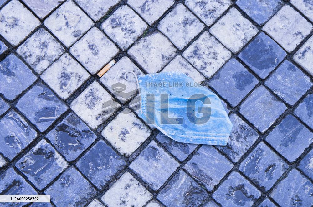 discarded face mask lies on the ground, pavement, pandemic, coronavirus, hazardous waste, fag end, cigarette stub