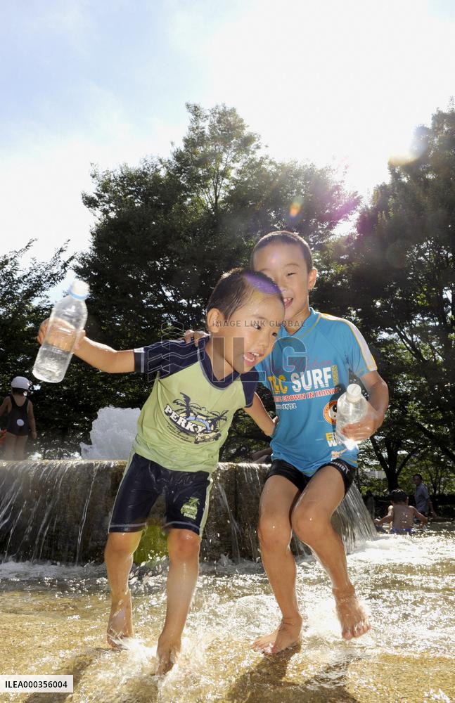Children play around water fountain under summer sun