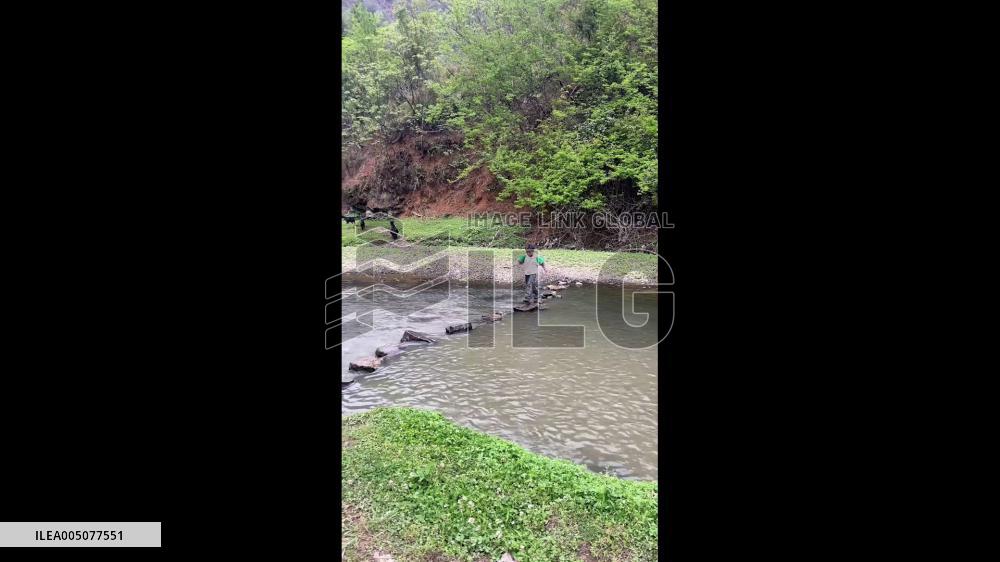 China: Young Shepherd Boy Carries Lamb Across Stream in Guizhou